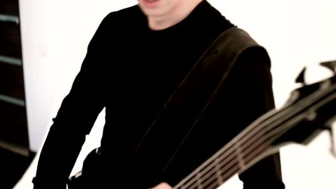 穿着黑色衣服的年轻男性音乐家，白色背景上有黑色低音吉他。低音吉他手表现音乐游戏