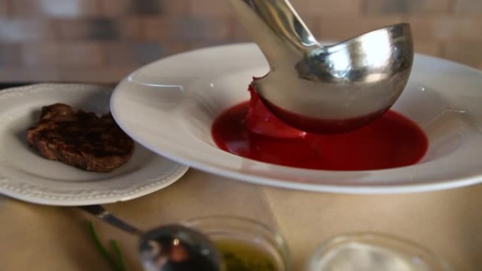 罗宋汤。将传统的俄罗斯罗宋汤倒入干净的白色盘子中的过程。