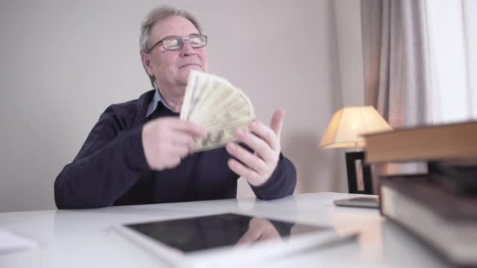 快乐的白人老人拿着一堆美元钞票，挥舞着现金。富裕成熟商人的肖像对收入感到满意。幸福、退休、生活方式、