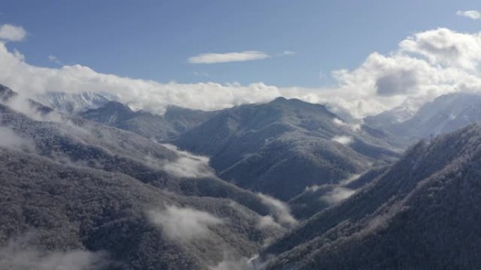 来自飞行无人机的多云天空景观上雪峰上的山村。鸟瞰图蓝雾天空背景上美丽的山谷。雪山和林地的壮丽景色