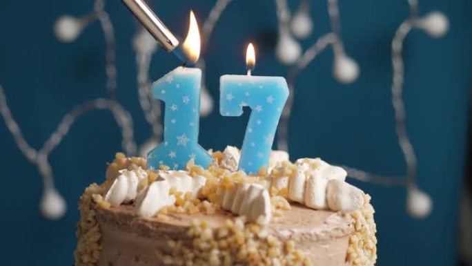 蓝色背景上有17个数字蜡烛的生日蛋糕。蜡烛着火了。慢动作和特写视图