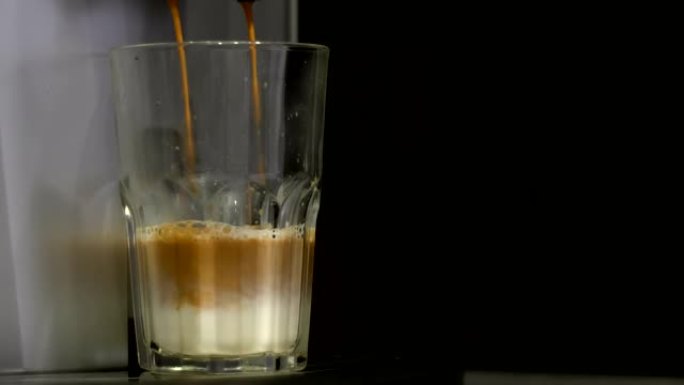 将咖啡机中的咖啡倒入装有牛奶的玻璃杯中。拿铁