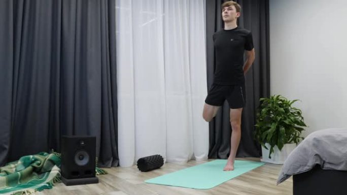 年轻的男运动员在家在瑜伽垫上伸展腿部肌肉。适合有动力的人在室内伸展。健身教练展示有氧运动和伸展运动。