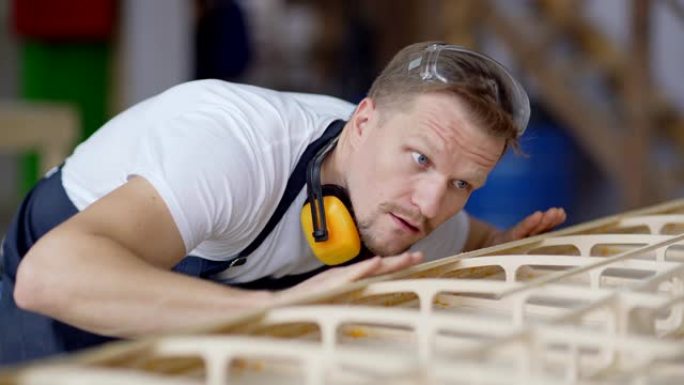 专注的专业木匠触摸放置在工作台上的精心手工制作的木船模型，以检查其是否足够光滑