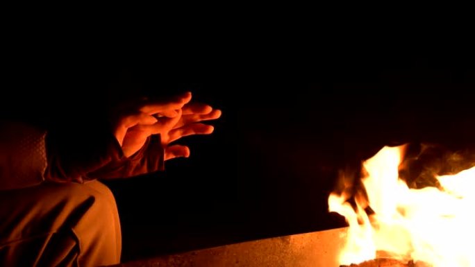特写在完全黑暗中的一个女人在明火上温暖双手。女人的手掌在夜晚的火旁