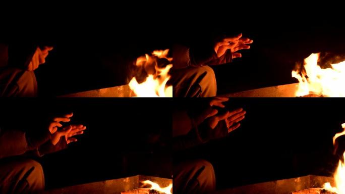 特写在完全黑暗中的一个女人在明火上温暖双手。女人的手掌在夜晚的火旁