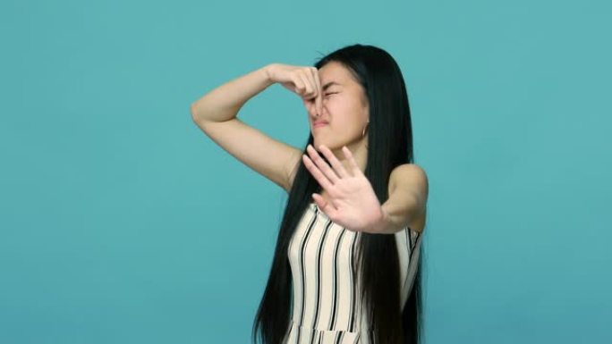 停止难闻的气味!不悦的亚洲女人，长长的黑发捏着鼻子，表现出拒绝的姿态