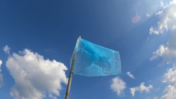蓝色的塑料旗迎风飘扬在蓝天白云的背景下。自制的旗子用来驱赶在稻田里吃稻谷的鸟。