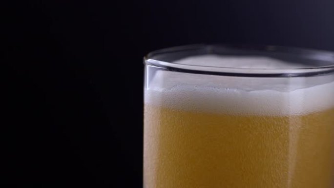 将新鲜和冰镇精酿啤酒放在玻璃中，黑色背景上有白色泡沫。在黑暗背景上流动的泡沫小麦或啤酒的宏观拍摄