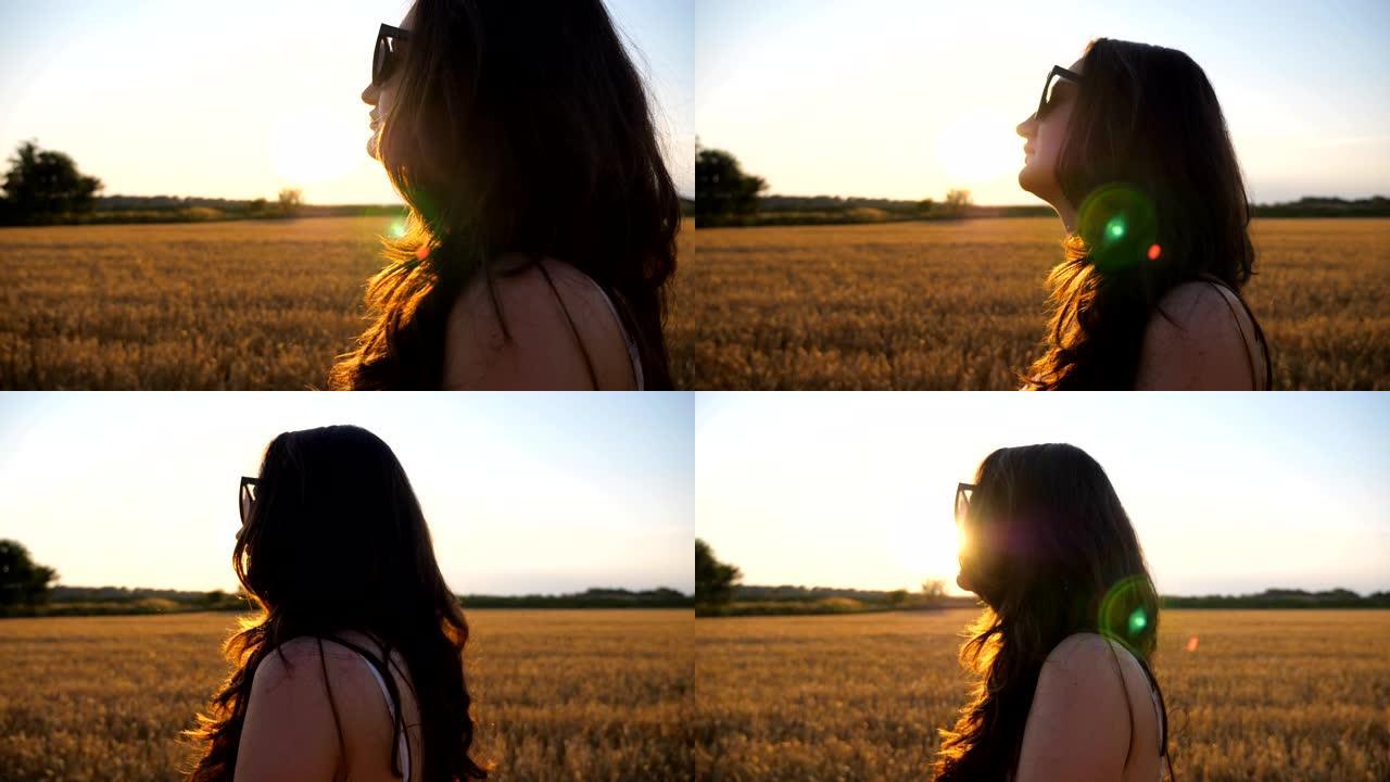 日落时分，美丽的女人走过麦田。无忧无虑的女孩在风景优美的自然环境中享受夏日夜晚和自由。在草地漫步的女
