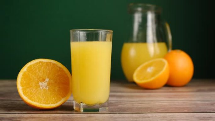 冰块落在橘子的木制桌子上的一杯橙汁或柠檬水中。用天然成分准备健康早餐。慢动作