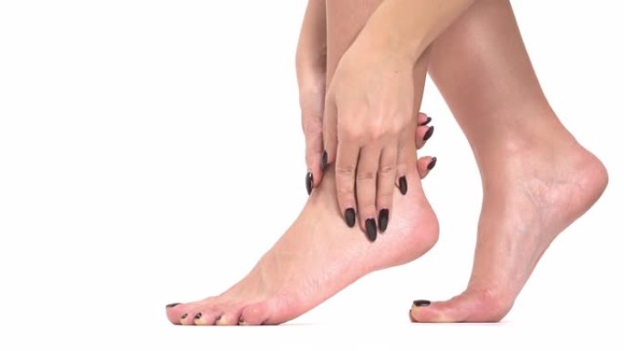 一个女人的特写镜头，时尚的黑色修指甲和修脚触摸她的腿和脚。身体护理概念。孤立，在白色背景上
