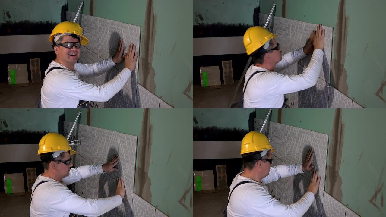 戴着黄色头盔的熟练工人在墙上铺瓷砖，看着相机