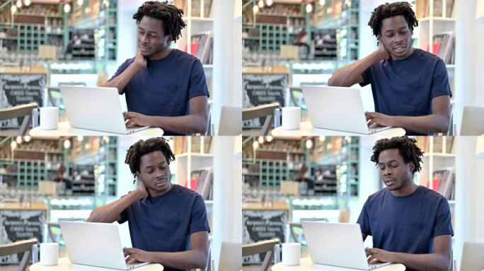 非洲男子颈部疼痛，在咖啡馆的笔记本电脑上工作