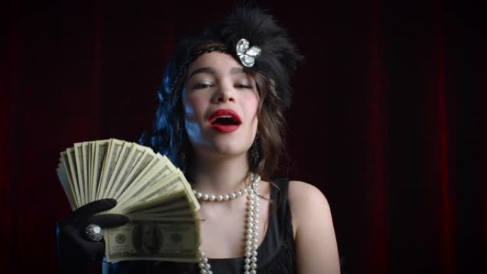 穿着盖茨比风格的富有奢华的女人像扇子一样挥舞着一捆美元钞票。复古，派对，复古时尚概念。