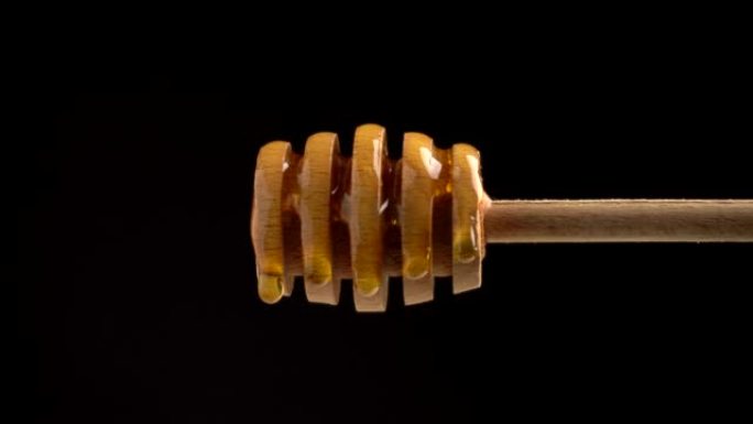 在用于蜂蜜的木勺上倒入新鲜液体黄色蜂蜜在黑色背景上特写
