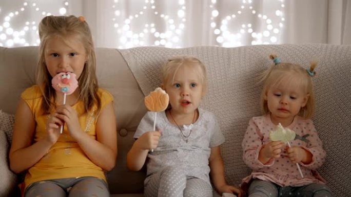 三个女孩坐在舒适的公寓沙发上吃棒棒糖