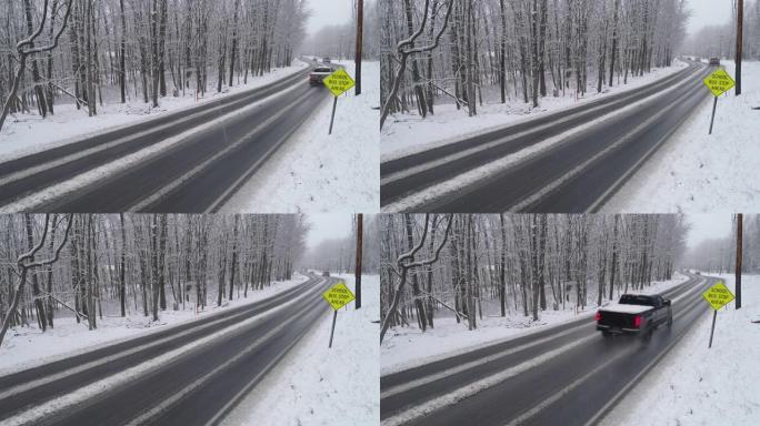 皮卡车和其他汽车在降雪下驾驶高速公路穿过森林。带有静态摄像机的无人机航拍视频。