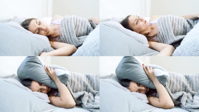 年轻恼怒的女人试图躺在床上睡觉。愤怒的女孩用枕头遮住耳朵，大声吵闹。