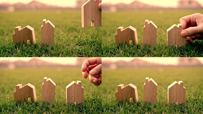 女人的手在绿草上选择迷你木房子模型，计划购买房地产，生态房子图标概念。