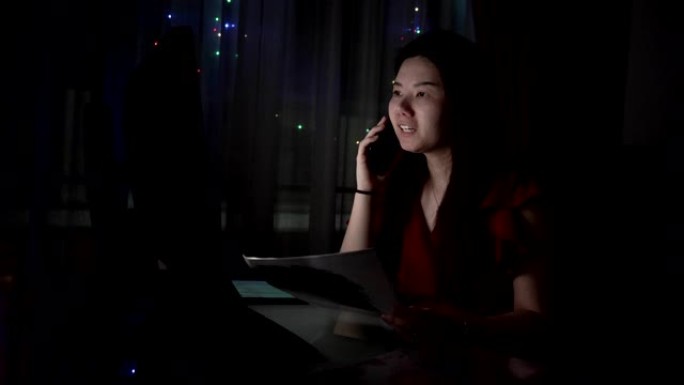 深夜，女工坐在办公室的笔记本电脑桌旁用手机聊天。