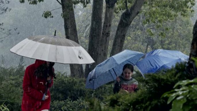 三个孩子的慢动作在雨中快乐奔跑，用雨伞的水坑