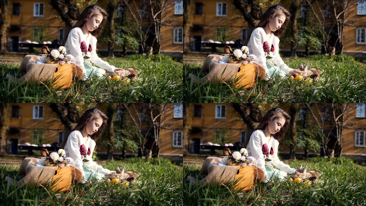 院子里的女孩坐在毯子上的草地上，拍拍复活节兔子。