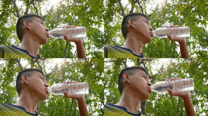 亚洲十几岁的男孩在公园慢跑后从瓶子里喝水。