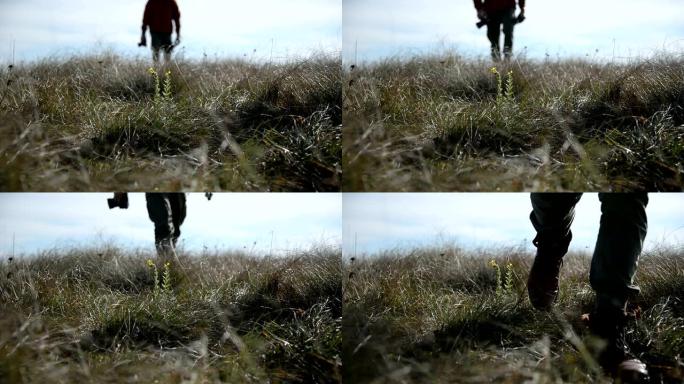 摄影师的脚的特写镜头，其轮廓超出了地平线，变成了散焦。一位摄影师走过一片野草