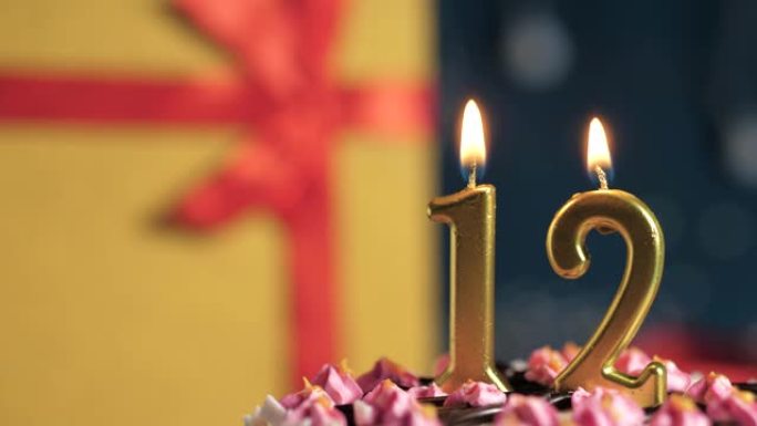 生日蛋糕12号点火器燃烧的金色蜡烛，蓝色背景礼物黄色盒子用红丝带绑起来。特写和慢动作