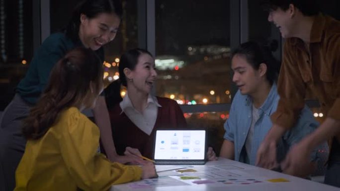 亚洲女性领导者和ux/ui设计师为平板电脑的移动应用界面线框设计在晚上的现代办公室鼓掌。在创意数字开