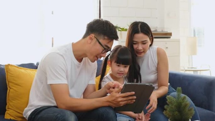 快乐的亚洲家庭在沙发/家庭游戏、教育平板电脑上共度时光