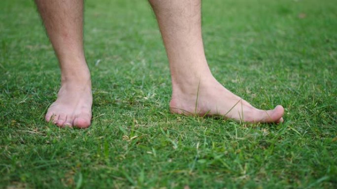 赤脚雄性在花园里新鲜切割的绿草上拍打脚趾