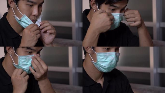 侧视图，Asain男性戴上医用防护口罩，坐在家里的灰色沙发上，自我护理，疾病预防，保健概念，健康问题