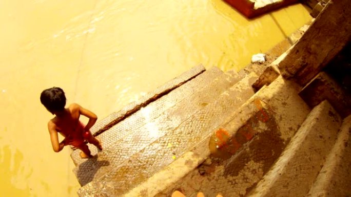 印度小男孩绑上他的缠腰布，上楼梯恒河的脏棕色水顶视图瓦拉纳西