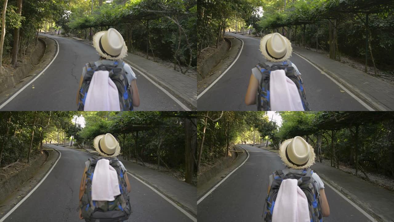 亚洲女性徒步旅行者背着背包穿过热带雨林的后视图。戴草帽的女人走在小路上。