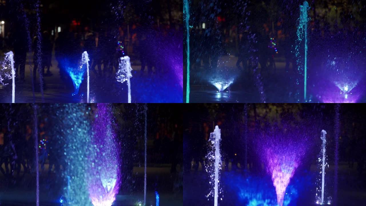晚上五颜六色的舞蹈喷泉。黑暗背景上的水流的慢动作特写镜头。无法识别的人剪影