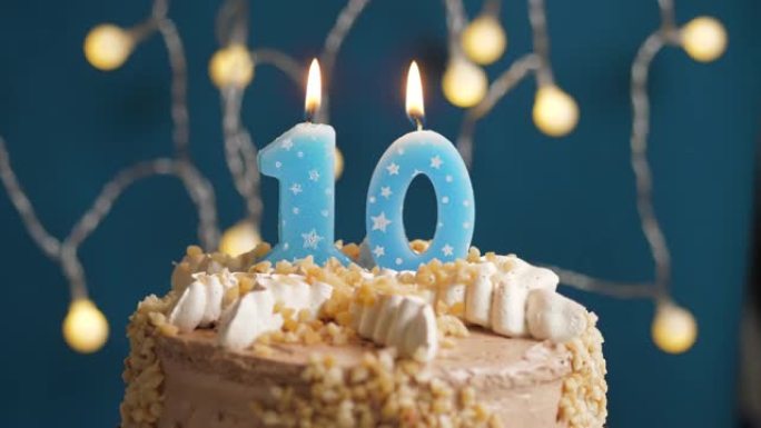 蓝色背景上有10号蜡烛的生日蛋糕。蜡烛吹灭了。慢动作和特写视图
