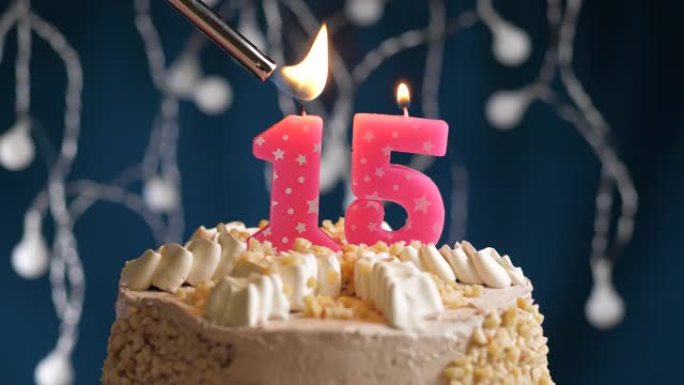 蓝色背景上有15个数字粉色蜡烛的生日蛋糕。蜡烛着火了。慢动作和特写视图