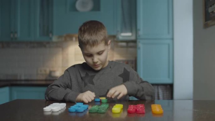 自闭症男孩在家里的桌子上按颜色分类塑料盖。自闭症孩子成排排列颜色帽子。自闭症学习。