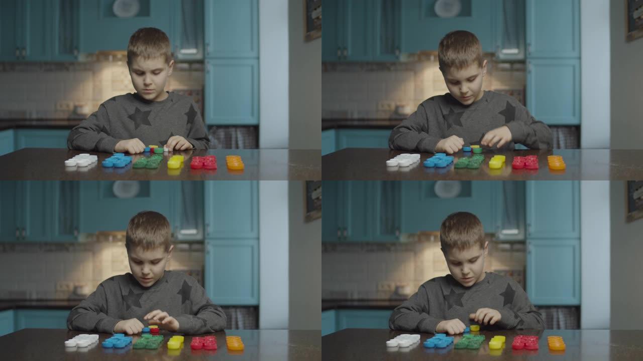 自闭症男孩在家里的桌子上按颜色分类塑料盖。自闭症孩子成排排列颜色帽子。自闭症学习。