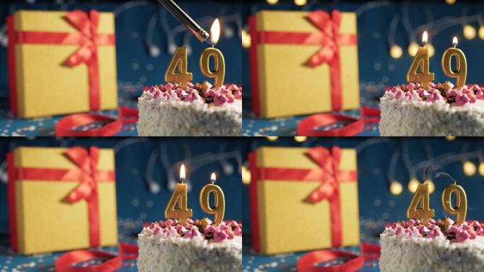 白色生日蛋糕编号49点灯燃烧的金色蜡烛，带灯的蓝色背景和用红丝带绑起来的礼物黄色盒子。特写