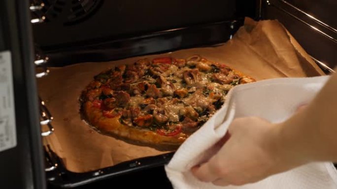女厨师从烤箱里拿烤披萨。在家做披萨，厨房。女性准备的披萨