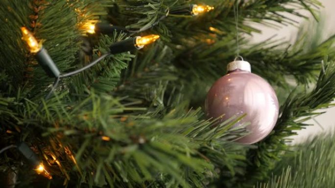 温暖的黄色圣诞灯泡和人造树枝上的粉红色摆设4K