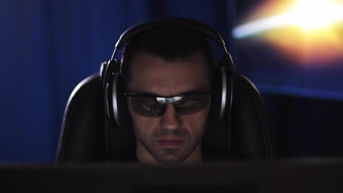 一个戴着耳机和3D眼镜的专心的人在黑暗的房间里看着电脑屏幕。
