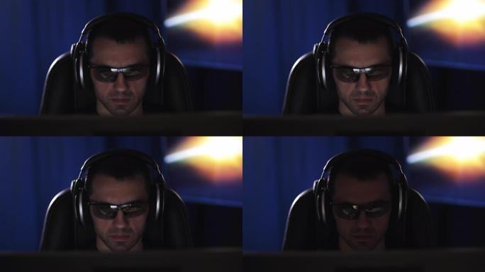 一个戴着耳机和3D眼镜的专心的人在黑暗的房间里看着电脑屏幕。