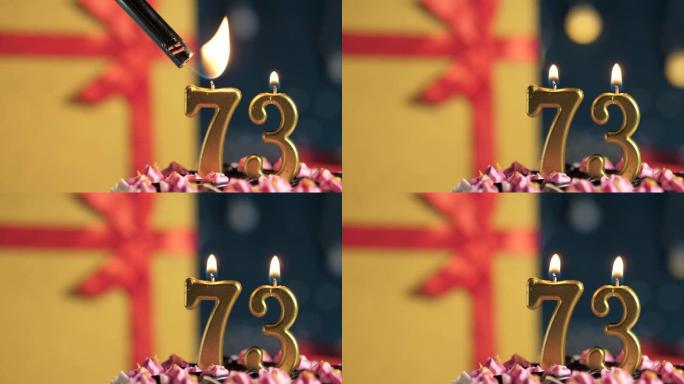 生日蛋糕编号73点灯燃烧的金色蜡烛，蓝色背景礼物黄色盒子用红丝带绑起来。特写和慢动作