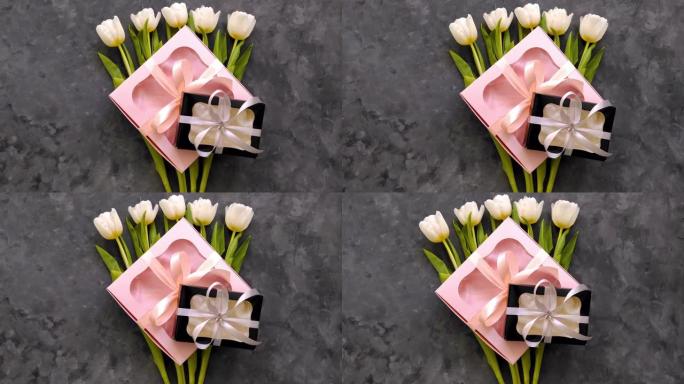 白色郁金香花与黑色和粉红色礼品盒在黑暗背景平躺着。4k视频。3月8日母亲节快乐