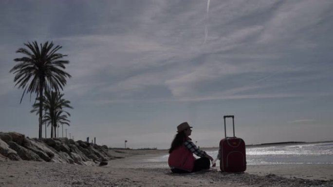 旅行女人带着手提箱坐在海边的海岸线上，旅行概念