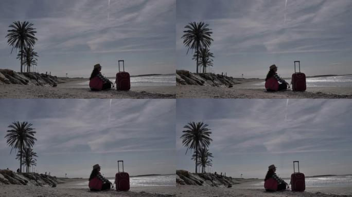 旅行女人带着手提箱坐在海边的海岸线上，旅行概念